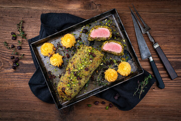 Fried mangalica pork tenderloin coated with crashed pistachio nuts, grated parmesan and chopped cranberries served with princess potatoes as close-up on a rustic black metal tray and carving set