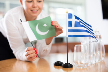 Employee of delegation prepares negotiating table - sets up the flag of Greece and Pakistan
