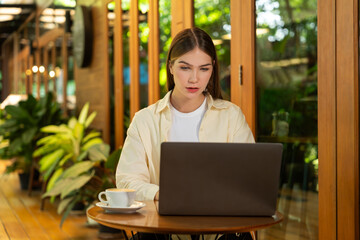 Young woman working on laptop at outdoor cafe garden during springtime, enjoying serenity ambient...