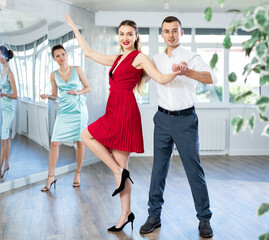 Smiling elegant young adult couple, bride and groom rehearsing sensual wedding dance in studio under guidance of professional female choreographer in bright studio..