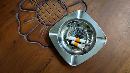 Silver ashtray, cigarette butts and ashes on a brown wooden table