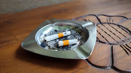 Silver ashtray, cigarette butts and ashes on a brown wooden table
