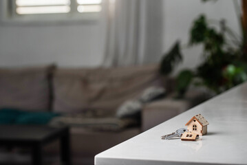 Keys with house shaped keychain on table on living room interior background. Concept of new homeownership, renting or leasing a property, and the process of purchasing a home, mortgage arrangements.