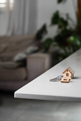 Keys with house shaped keychain on table on living room interior background. Concept of new homeownership, renting or leasing a property, and the process of purchasing a home, mortgage arrangements.