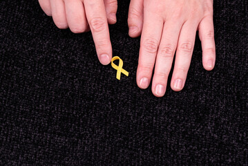 Hands placing a yellow ribbon pin on fabric, the international symbol of advocating for the return...
