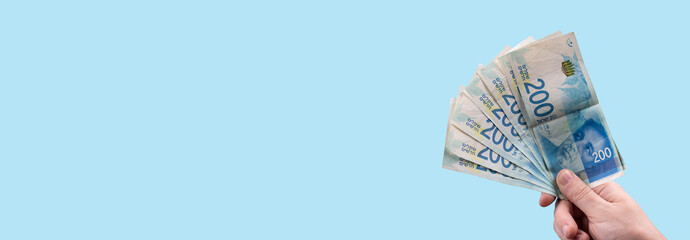 Hand holding stack of cash bills, New Israeli Shekels (NIS), representing financial wealth, abundance, and prosperity in Israel. - obrazy, fototapety, plakaty