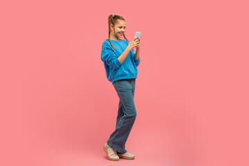 Young girl smiling at smartphone on pink background