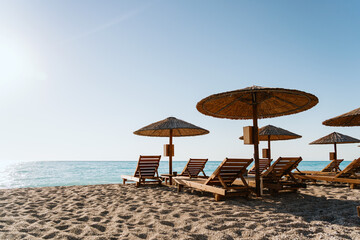 Inviting beach scene with straw umbrellas and wooden chairs facing the blue sea on a sunny day,...