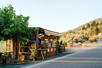 A charming little roadside stand offers local goods under the bright summer sun, nestled in lush...