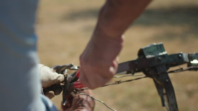 Two men work together to repair a barbed wire fence in a cattle pasture