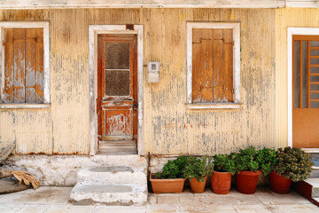 Old rustic house exterior with peeling paint on door and shutters, and potted green plants on the...