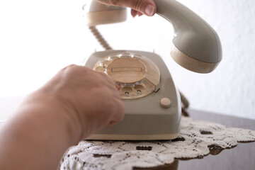 mature female hand removing Handset, rotating Dialer on Old white Rotary Telephone with Disc Dial with finger, putting retro phone reciver down, hanging up, calls helpline, psychological support - obrazy, fototapety, plakaty