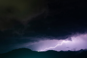 lightning over the mountains surrounded with black and violet clouds