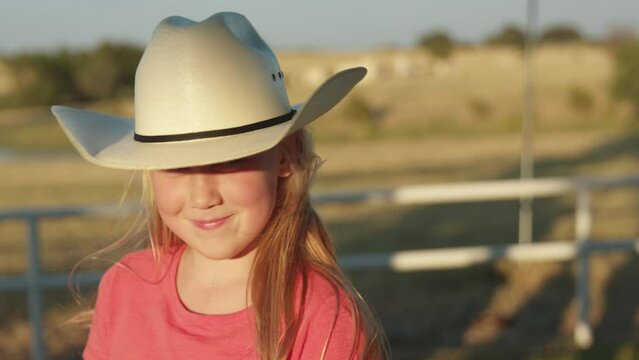 A young farmer girl wearing a cowboy hat looks up and smiles