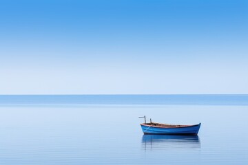 A small blue boat sits in the middle of a large body of water. The sky is clear and blue, and the water is calm. The scene is peaceful and serene, with the boat as the only point of interest