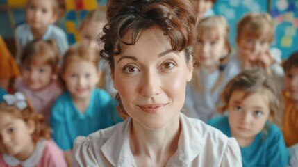 Fototapeta premium Beautiful professional female teacher of nursery school or kindergarten looking at camera while standing against group of little learners