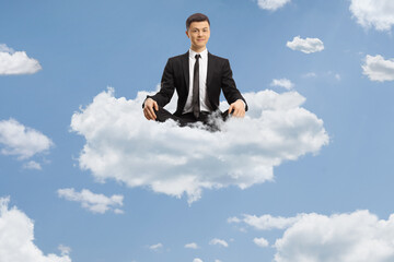 Young man in a black suit sitting with crossed legs and meditating on a cloud