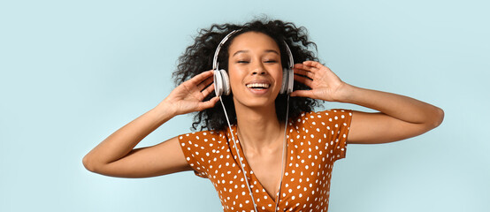 Young African-American woman listening to music on color background