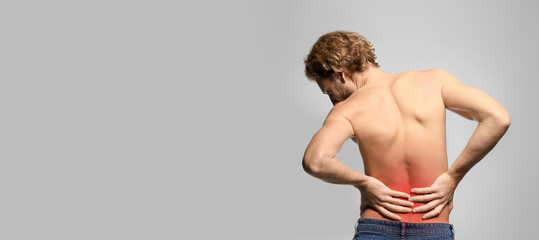 Young man suffering from back pain on light background
