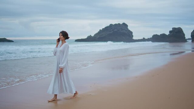 Beautiful woman calling smartphone at ocean beach. Relaxed lady walk sandy coast