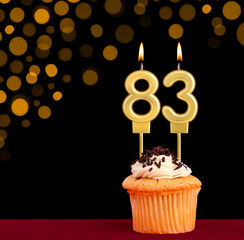 Birthday candle with cupcake - Number 83 on black background with out of focus lights