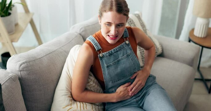 Woman, couch and pain with menstruation in home, thinking and massage abdomen in living room. Above, girl and person with stomach cramps for digestion, virus or bloated with constipation at apartment