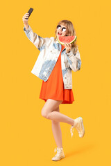 Young woman with fresh watermelon taking selfie on orange background