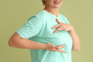 Mature woman checking her breast on green background, closeup. Cancer awareness concept