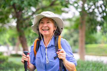 portrait happy asian senior woman with trekking poles and backpack wears hat in the national park for hiking,active elderly female,lifestyle,activity,healthy,adventure in nature