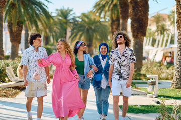 A diverse group of tourists, dressed in summer attire, strolls through the tourist city with wide...