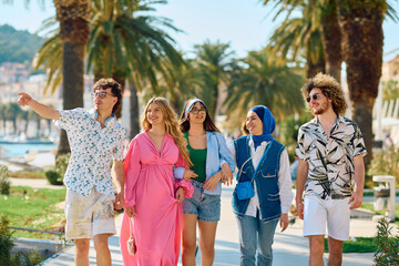 A diverse group of tourists, dressed in summer attire, strolls through the tourist city with wide...