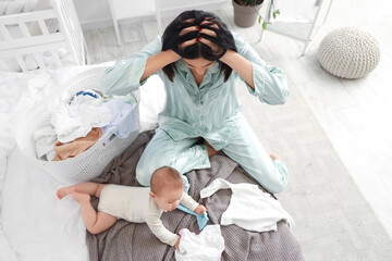 Young woman with her baby and laundry suffering from postnatal depression in bedroom - obrazy, fototapety, plakaty