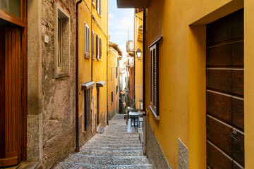 A narrow cobblestone alley with steps leading to the lake on a steep staircase with shops and cafes in the historic old town of Bellagio, Italy, on the shores of Lake Como.