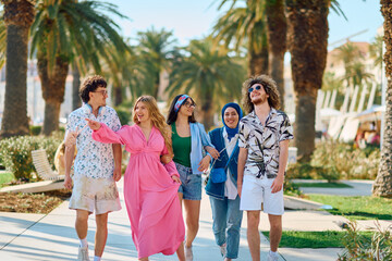 A diverse group of tourists, dressed in summer attire, strolls through the tourist city with wide smiles, enjoying their sightseeing adventure - obrazy, fototapety, plakaty