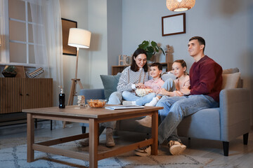 Happy family with popcorn watching TV on sofa at home in evening