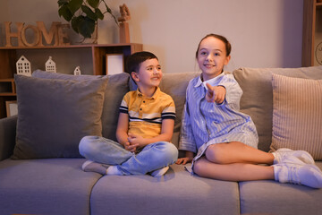 Little children watching TV on sofa at home in evening