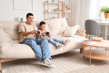 Happy father with his little son playing video game on sofa at home