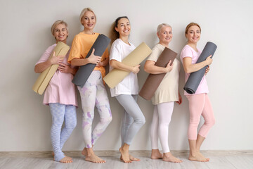 Group of mature women with yoga mats near light wall