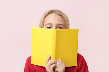 Cute little boy with yellow book on pink background