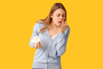 Young woman with tissue suffering from allergy on yellow background