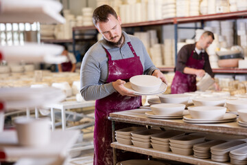 Young male factory worker posing with ceramic tableware blanks
