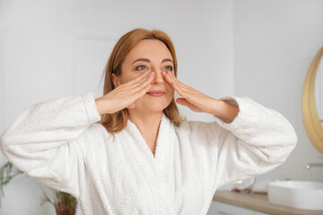 Beautiful happy mature woman in bathrobe doing face building exercise at home
