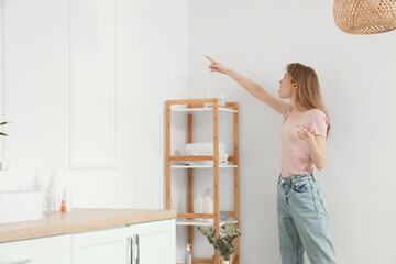 Shocked young woman pointing at mold on wall in bathroom