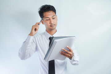 Young Asian business man showing thinking gesture while holding pen and note book
