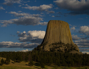 Devils Tower in Wyoming photographed in evening light with fluffy summer clouds in the blue sky.