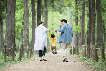 A family walking in good harmony, smiling and holding hands through fresh greenery and beautiful...