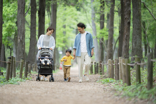 A Japanese (Asian) family of four walking in fresh greenery and beautiful greenery, smiling, holding hands, and getting along well. Image of insurance and leisure outings.