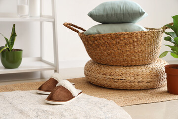Pair of soft slippers on rug near basket with pillows