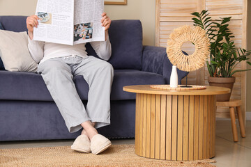 Man in soft slippers resting on sofa and reading newspaper at home