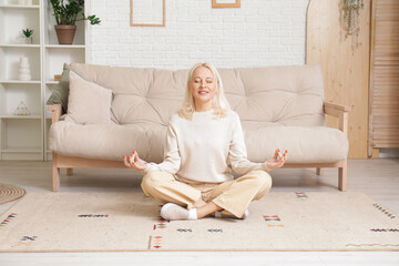 Mature woman meditating on carpet at home